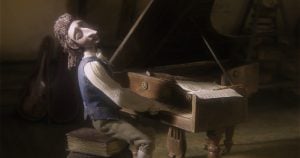 ‘Hoffmaniada’ Blu-Ray Review – A Dreamy, Overlooked Stop-Motion Fairy Tale A stop-motion puppet character plays a grand piano with sheet music, seated on a stack of books in a dimly lit room.