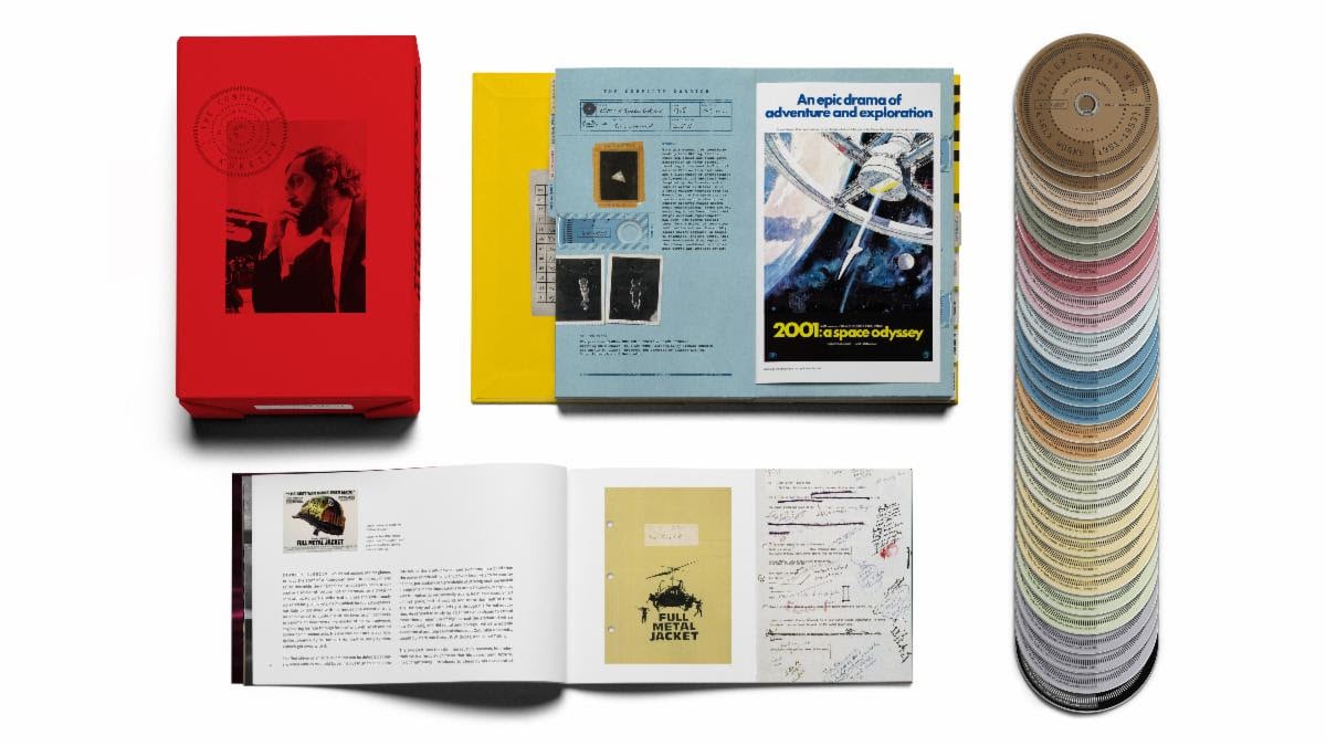 A red box set, an open booklet, posters, documents, and a spread of color swatch discs are arranged on a white background.