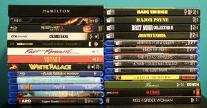 No Streaming Required: Physical Media Spotlight For The Week Of June 16th A collection of various Blu-ray and DVD movie cases stacked in two columns against a blue background.
