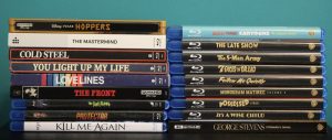 A collection of DVD and Blu-ray movie cases stacked in two columns against a teal background, showing various film titles on their spines.
