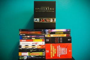 A stack of DVD and Blu-ray movie cases, topped with a box labeled "Steven Spielberg: The Spotlight Collection," set against a teal background.
