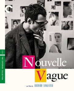 A man in glasses and a suit jacket stands in front of a wall covered with black-and-white photos; the text reads "Nouvelle Vague," styled in colorful blocks.