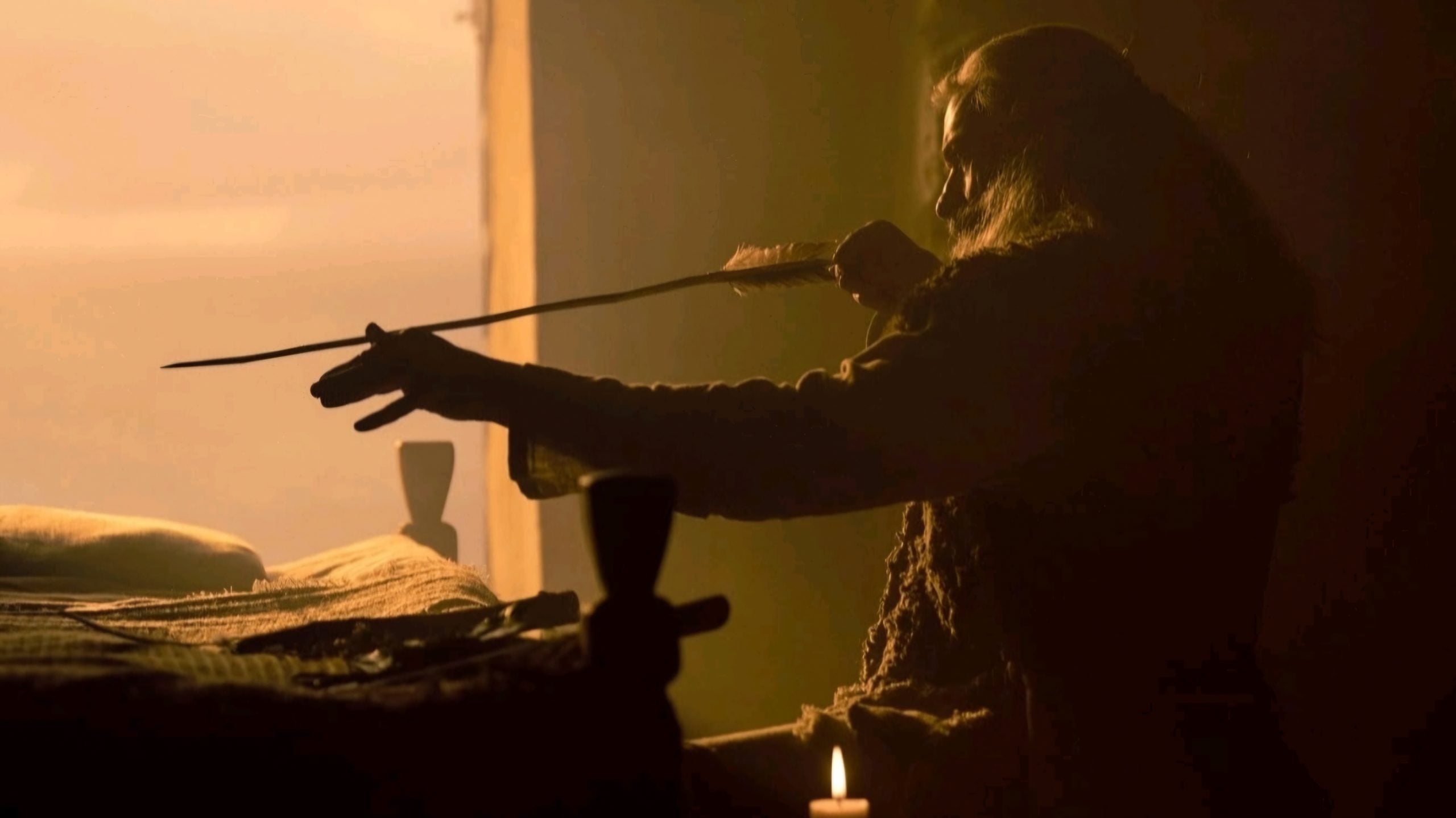 A person sitting indoors draws an arrow on a bow, illuminated by warm, dim light from a window and a candle on the table.