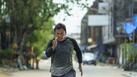 ‘The Furious’ (2026) 4K UHD Blu-Ray Review – A Deliriously Brutal Action Extravaganza A man in a dark long-sleeve shirt runs intensely down an empty street during the day, with trees and buildings in the background.
