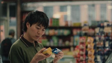 A person stands in a store aisle, holding and comparing two packaged food items while looking at them closely. Shelves with various products are visible in the background.