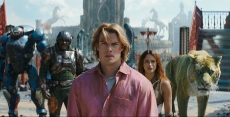 Amazon MGM To Release The Adventure Epic ‘Masters Of The Universe’ On 4K UHD Blu-Ray This October A man in a pink shirt stands in front of a woman, a large armored figure, a tiger, and another armored person in a futuristic city setting.