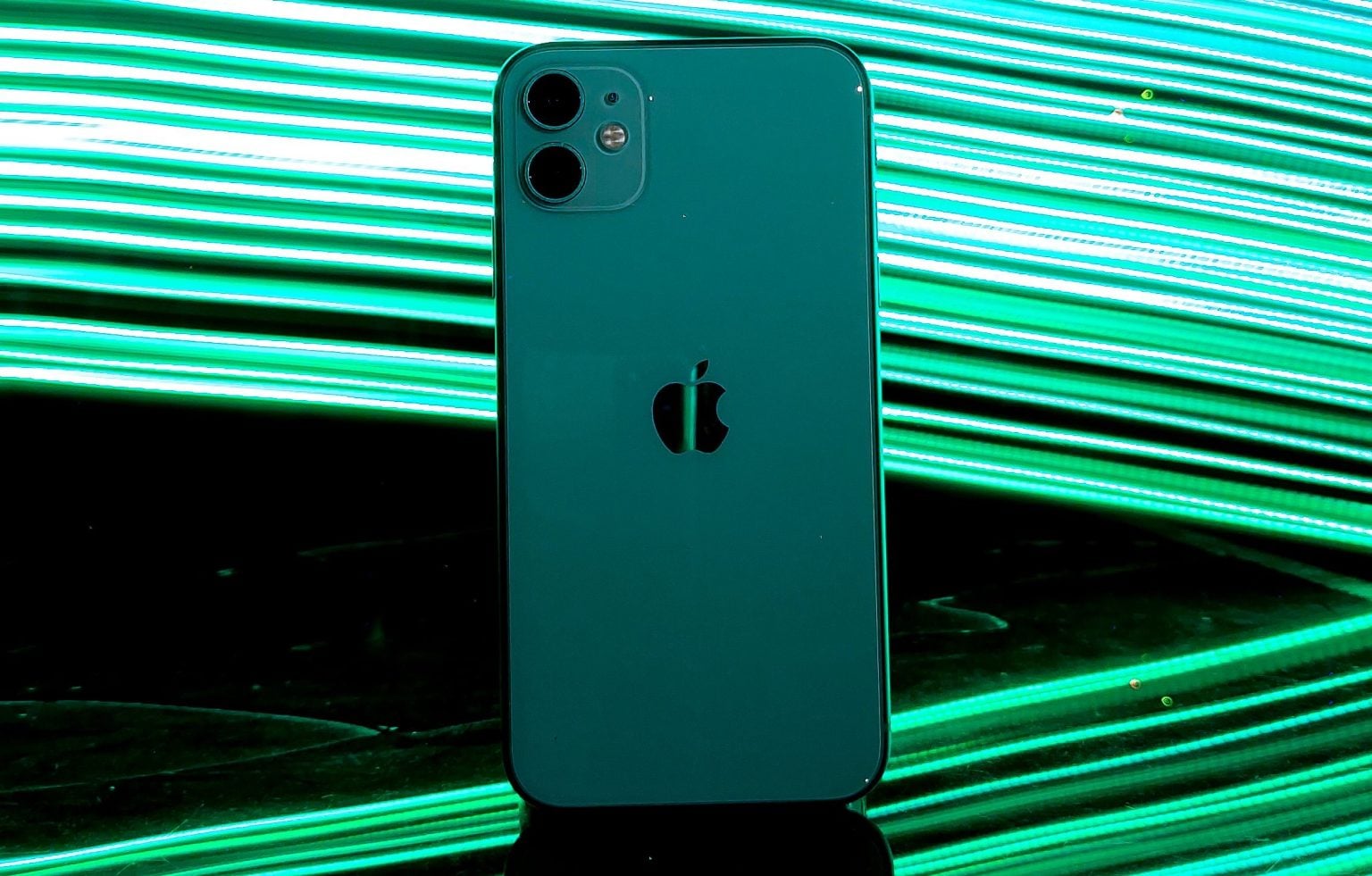 A green iPhone stands upright on a reflective surface with bright green light streaks in the background.