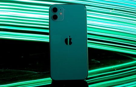 Should I Get An iPhone 17 or Wait For 18? A green iPhone stands upright on a reflective surface with bright green light streaks in the background.