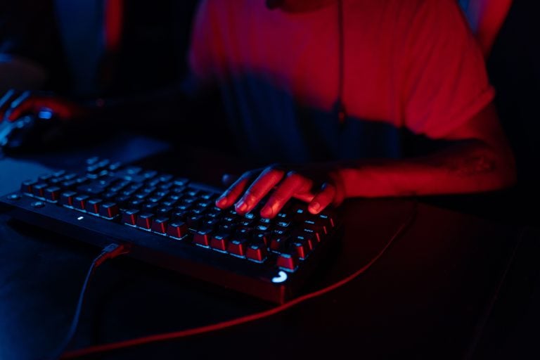 Understanding Drop Rates on CS2 Case Opening Sites Person typing on an illuminated mechanical keyboard in a dimly lit room, with red and blue lighting highlighting their hands and shirt.