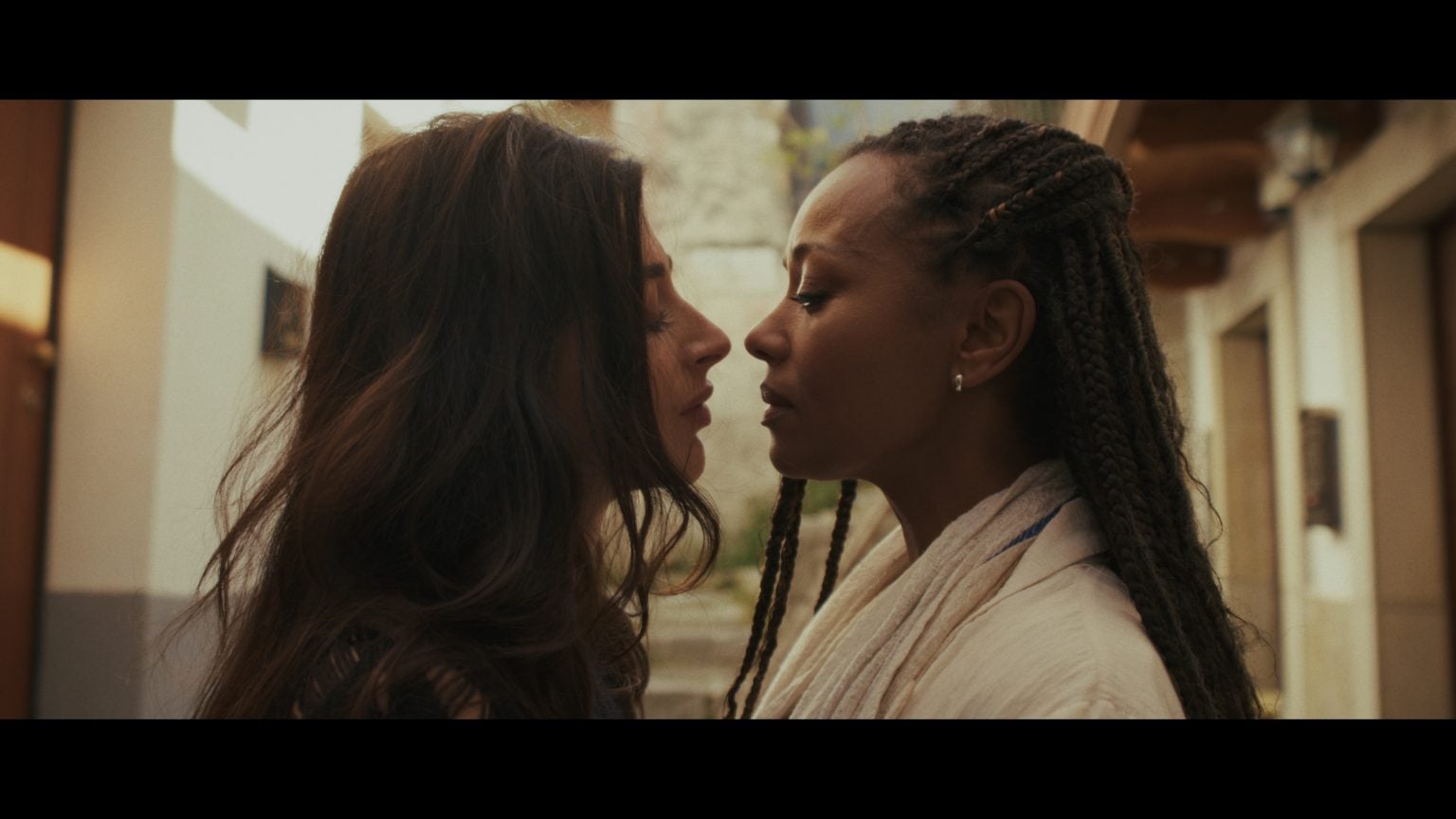 ‘A Year In London’ Movie Review – The Art Of Simple Loving Two women stand very close, facing each other, with calm expressions in an outdoor setting, suggesting an intimate or emotional moment.