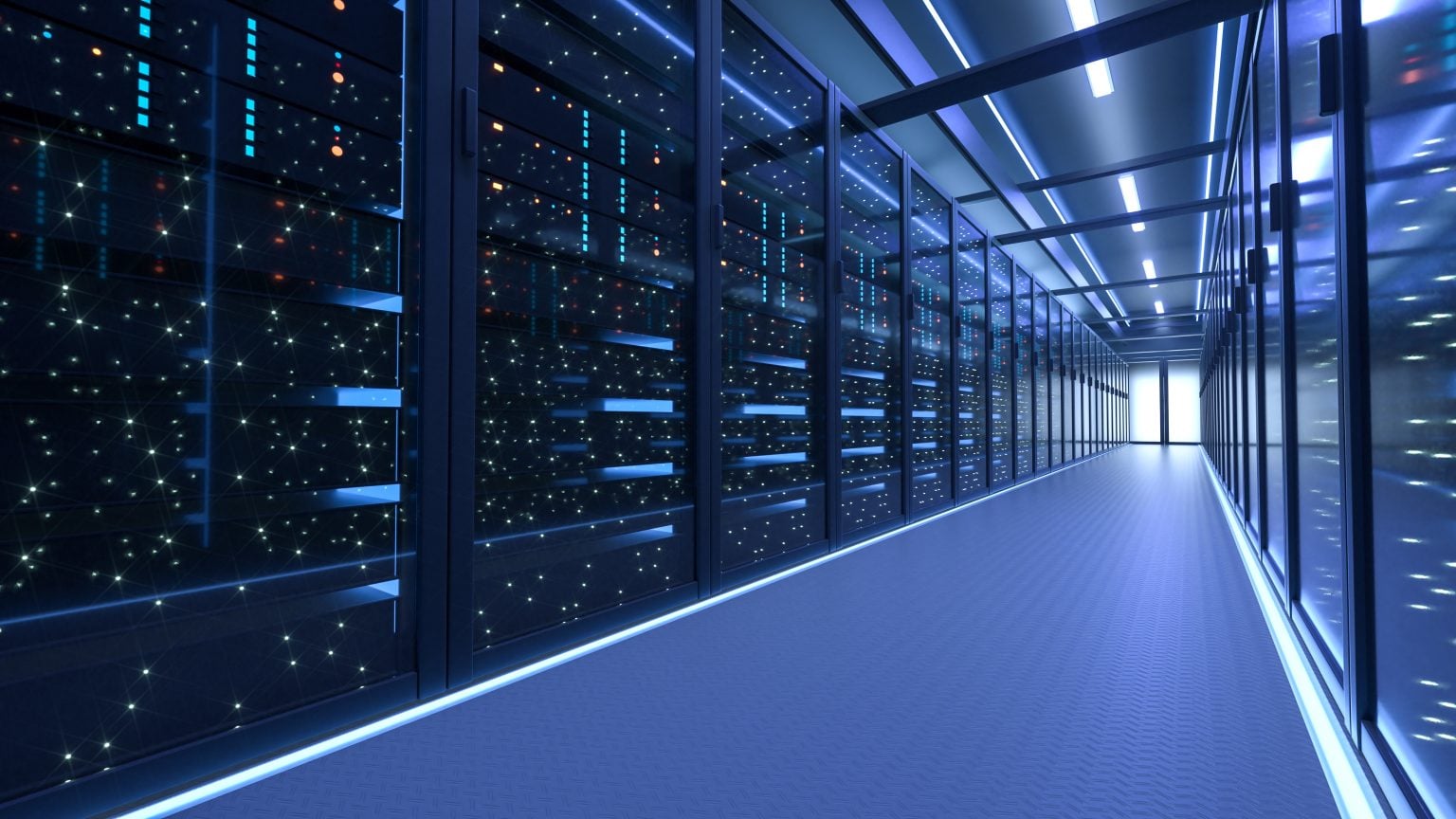 Why Modern Data Centers Require A New Build Strategy A brightly lit hallway in a modern data center, lined with server racks filled with illuminated equipment and cables, leading to a distant exit.