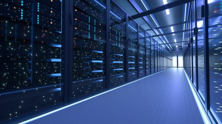 A brightly lit hallway in a modern data center, lined with server racks filled with illuminated equipment and cables, leading to a distant exit.