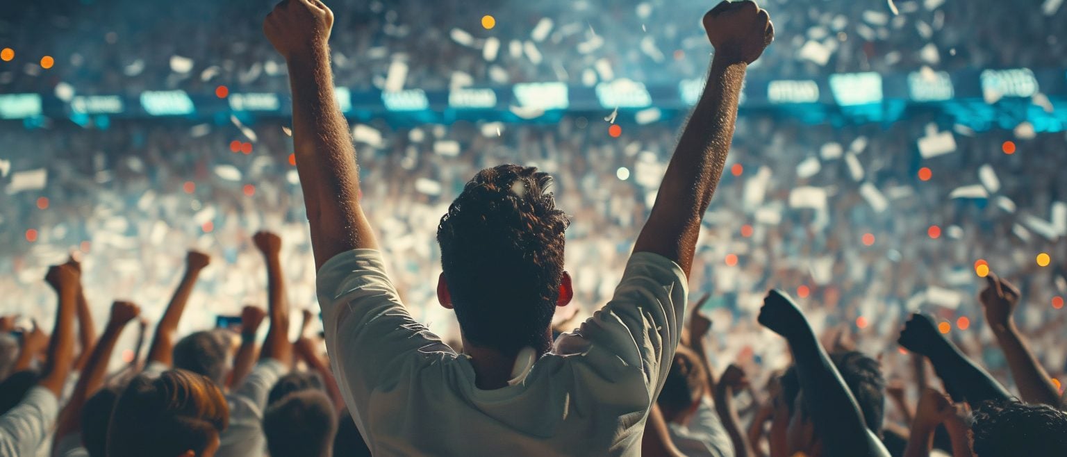 How Global Sporting Events Influence Local Fan Engagement A crowd of people in a stadium celebrate with raised arms and confetti falling, as one person stands prominently in the foreground facing the audience.
