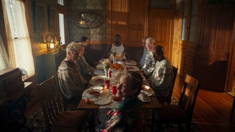 Alisa Kobyliatskaia on Boloto, Soviet Lenses, Dark Fantasy, And Building A Cinematic World Between Cultures Seven people sit around a dining table set for a meal in a warmly lit room, with plates, glasses, and flowers arranged on the table.