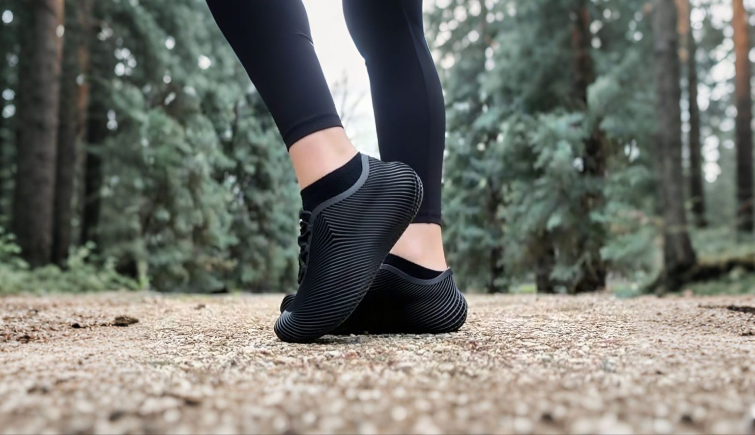Best Summer Walking Shoes For Hot Weather Person wearing black athletic shoes and leggings standing on a gravel path in a forest, with trees visible in the background.