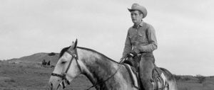 ‘Hud’ Criterion Collection 4K UHD Blu-Ray Review – Paul Newman Illuminates The Screen In One Of His Best Performances A man in a cowboy hat and denim shirt rides a horse across open terrain. Two riders are visible in the distance under a cloudy sky.