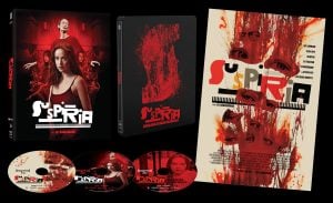 A Suspiria film box set with a DVD case, steelbook, and poster, all featuring red and black artwork, plus three discs with matching designs.