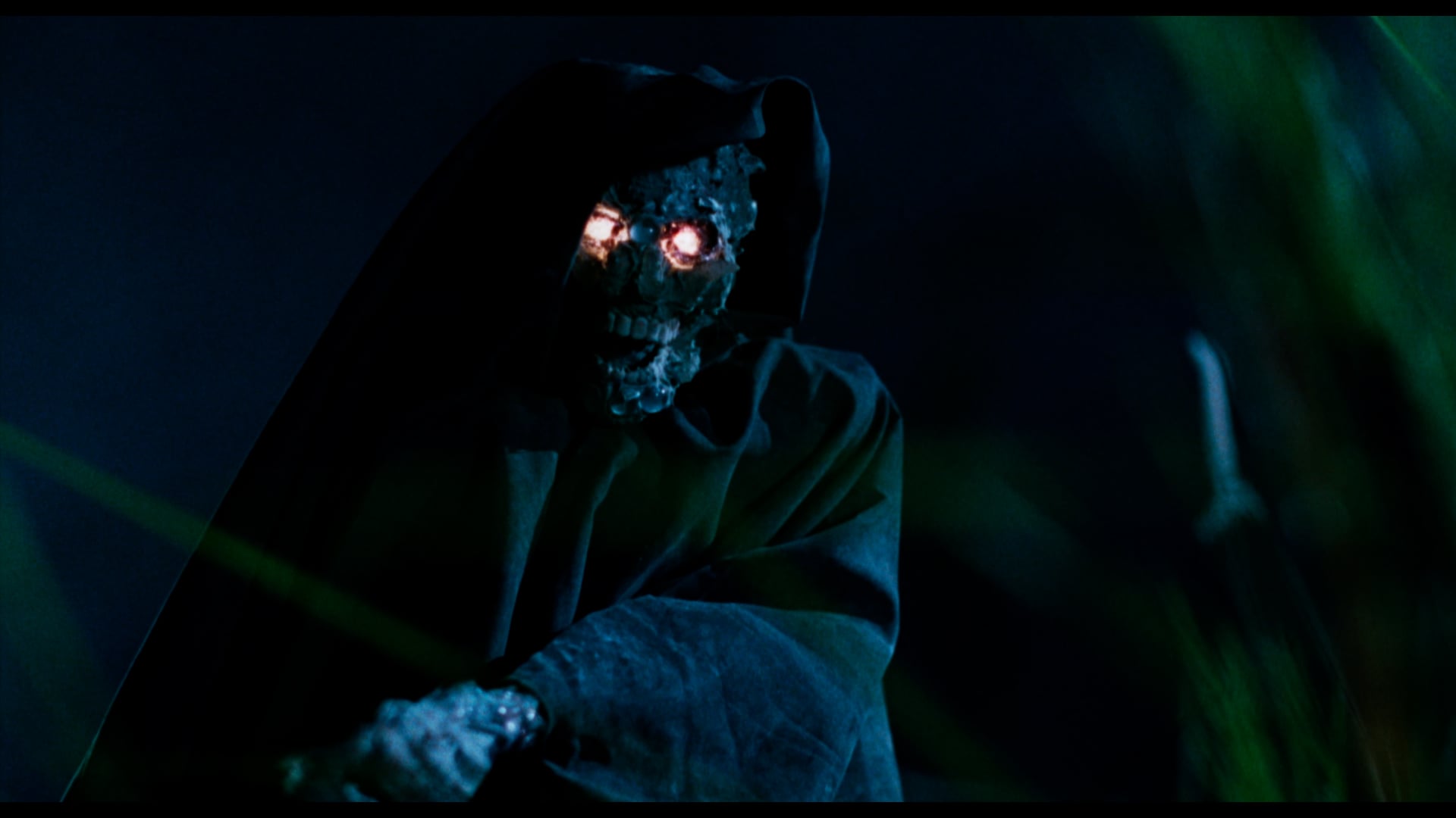 A hooded, decaying skeletal figure with glowing red eyes stands in the dark, partially concealed by shadows and foliage.