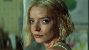 A woman with short blonde hair and visible bruises on her face looks over her shoulder with a serious expression.