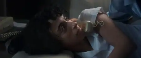‘Night Nurse’ (2026) Review – Seduction By Playing Helpless A woman with curly hair lies on her side holding a beige corded telephone to her ear, looking upward with a serious expression.