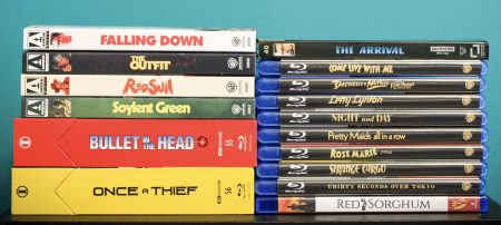 No Streaming Required: Physical Media Spotlight For The Week Of July 7th Eleven DVD cases stacked vertically on the left and ten Blu-ray cases stacked vertically on the right, all with visible movie titles, against a teal background.