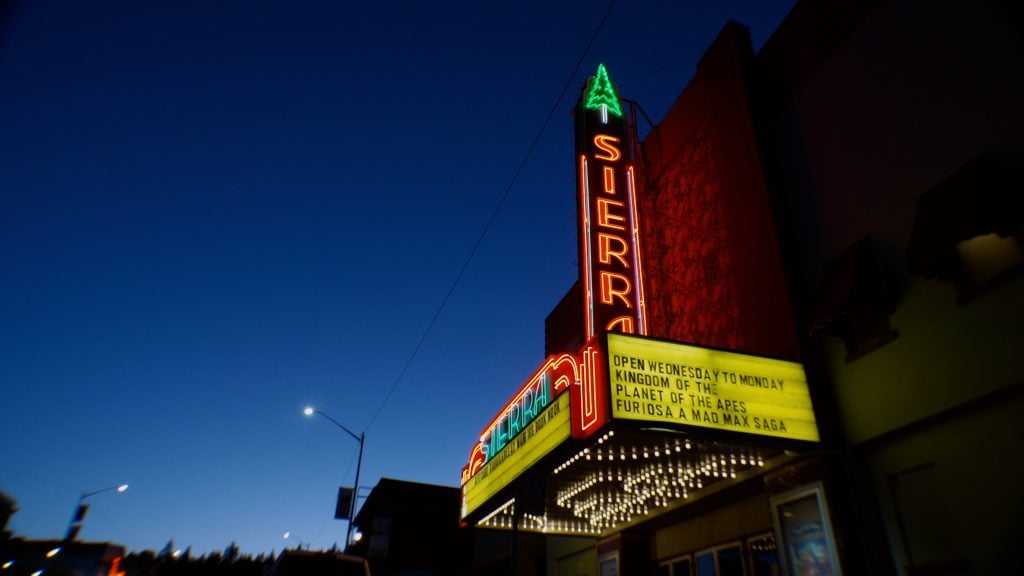 Neon-lit Sierra theater marquee at dusk displays showtimes for "Kingdom of the Planet of the Apes" and "Furiosa: A Mad Max Saga.