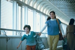 A woman and a child walk hand in hand down a covered pedestrian walkway, both smiling and carrying shopping bags.