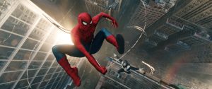 Spider-Man swings through a city with tall buildings, while another costumed figure follows behind, both high above the street below.