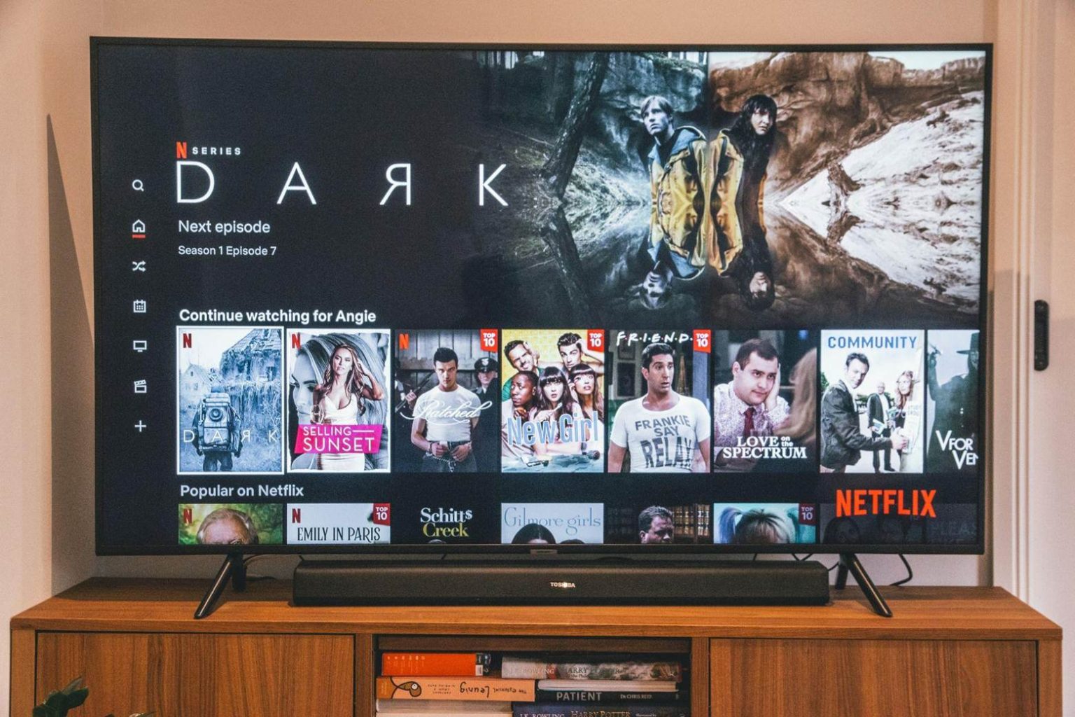 A TV screen displays the Netflix homepage featuring the series “Dark” along with recommendations and trending shows, set on a wooden media console.