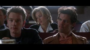 ‘Nightwatch’ (1997) 4K UHD Blu-Ray Review – An Amazing Ensemble Justifies This Americanized Thriller Three people sit in a lecture hall. Two men are seated in the foreground, while a woman sits behind them, looking down. Other students appear out of focus in the background.