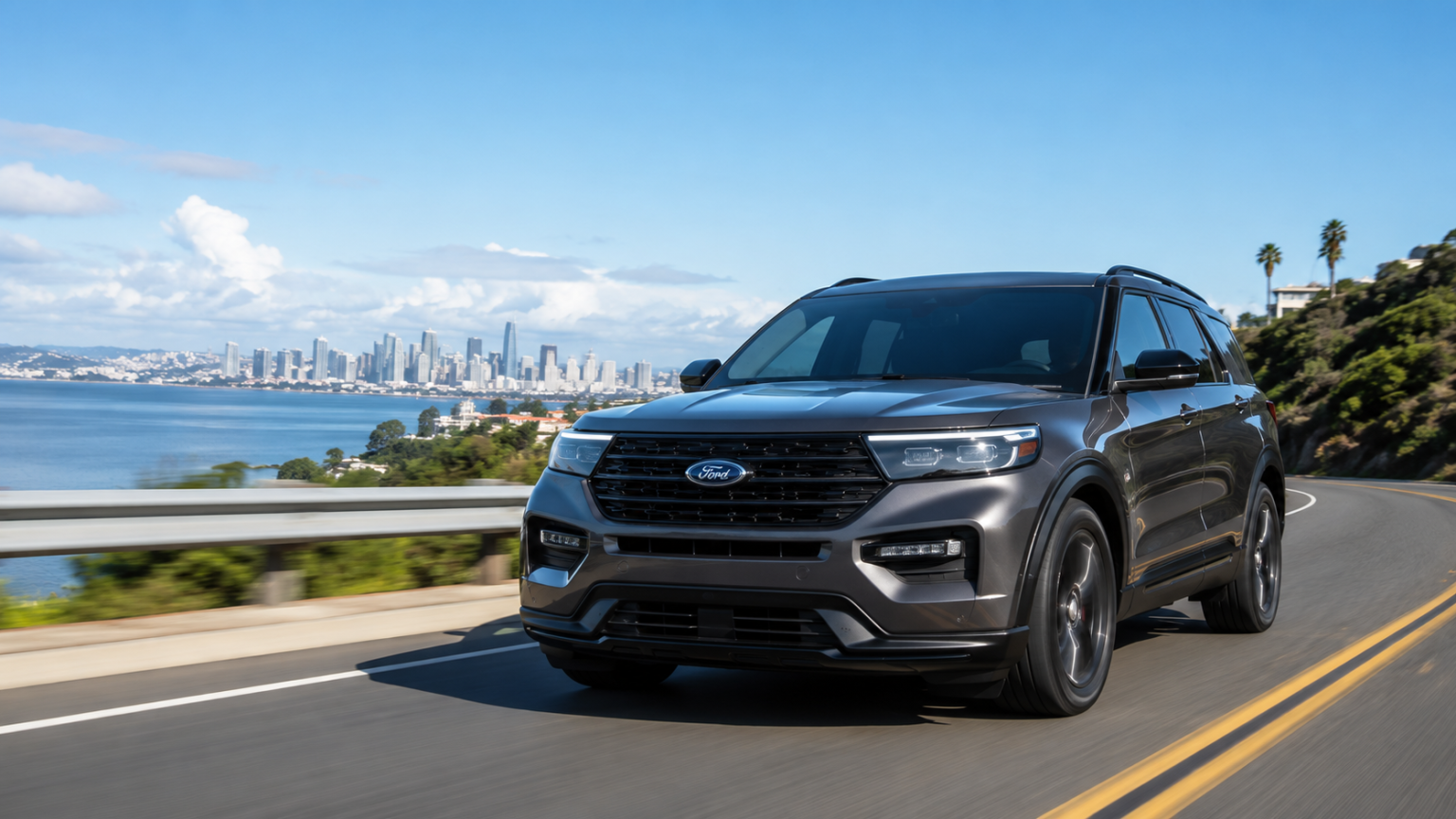 A gray Ford SUV drives on a coastal road with a city skyline and water in the background under a sunny blue sky.