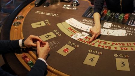 A person plays blackjack at a casino table, holding cards while a dealer displays two face-up cards. Chips are stacked on the table.
