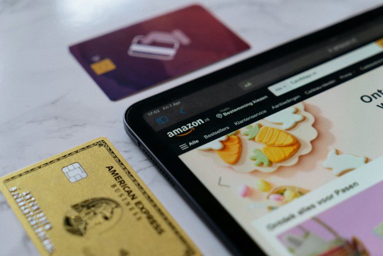 Technical SEO For Ecommerce Sites: Common Issues That Hurt Product Visibility A tablet displaying the Amazon website sits on a white surface next to a gold American Express card and a partially visible purple card.