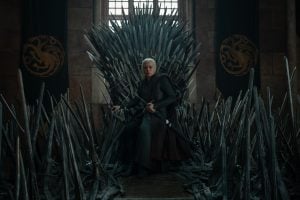‘House of the Dragon’ Season 3 Ep 2 Review: A Goal Years In The Making A person in medieval armor sits on an elaborate iron throne made of swords, with banners featuring dragon symbols on the walls behind.