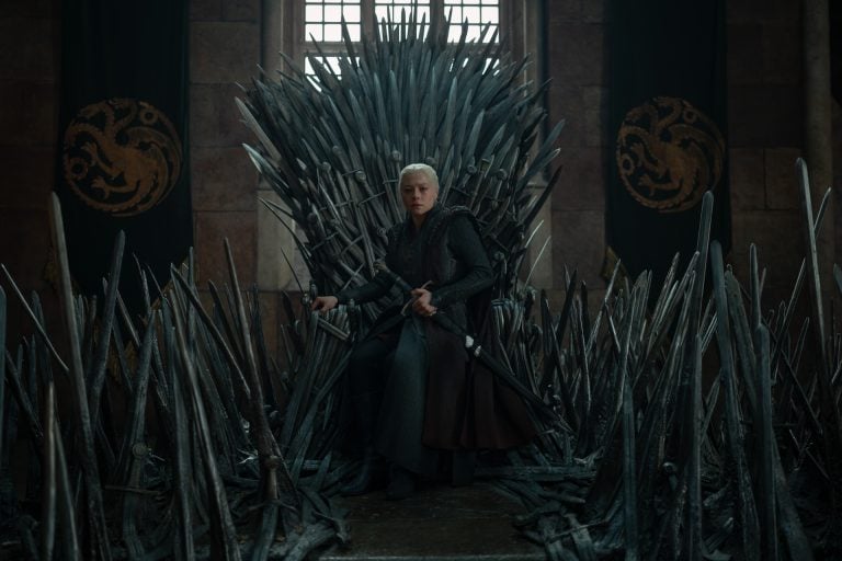 ‘House of the Dragon’ Season 3 Ep 2 Review: A Goal Years In The Making A person in medieval armor sits on an elaborate iron throne made of swords, with banners featuring dragon symbols on the walls behind.