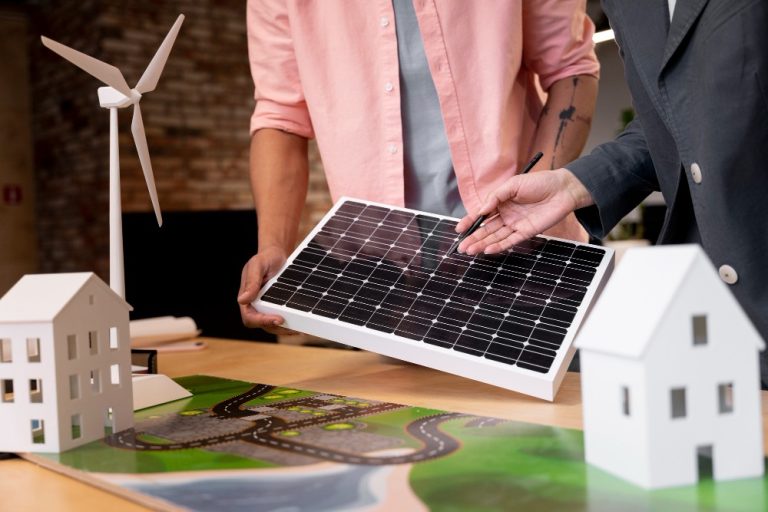Portable Solar Panels vs Rooftop Solar Systems: Which One Fits Your Home? Two people examine a solar panel next to scale models of houses, a wind turbine, and a map, suggesting a discussion about renewable energy or sustainable planning.