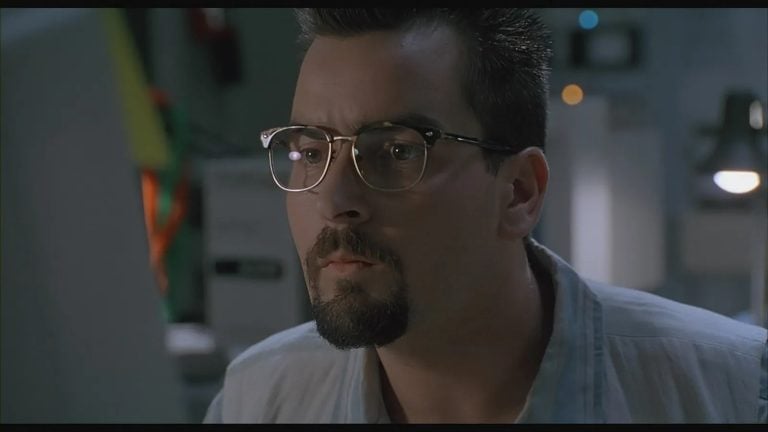 ‘The Arrival’ (1996) 4K UHD Blu-Ray Review – Charlie Sheen Searches For The Truth In This Engaging Alien Outing A man with glasses and a goatee closely looks at a computer screen in a dimly lit room.