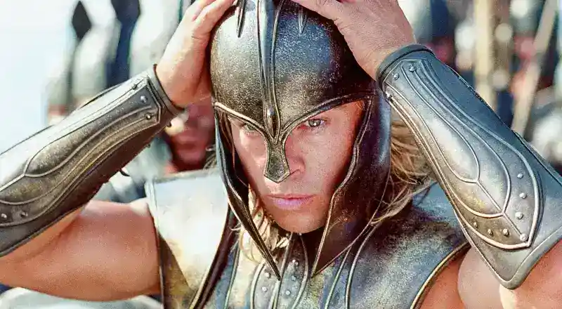 A warrior in gold armor and helmet adjusts his headgear, with other similarly armored soldiers in the background.