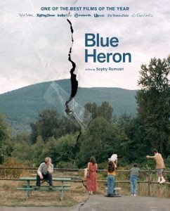 A group of people stands near a wooden fence overlooking a lake and mountains; a torn effect divides the image with the title “Blue Heron” and film credits displayed.