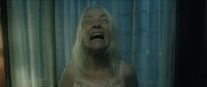 Brainstorm Media Debuts Clip For One-Shot Horror Film ‘Bury The Devil’ To Celebrate Release An older woman with long white hair stands in front of curtains, tilting her head back with her eyes rolled upward and mouth wide open in a scream.