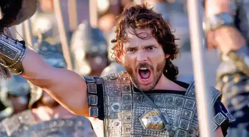 A man in ornate armor shouts with his mouth open, raising his arm amid a group of armored soldiers in the background.