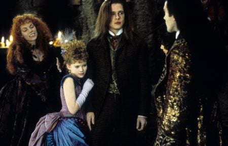 Warner Bros. To Release Tom Cruise & Brad Pitt’s ‘Interview With The Vampire’ On 4K UHD Blu-Ray This September Four people in elaborate, old-fashioned costumes stand indoors; three appear tense while one woman in blue clings to the man in the center.