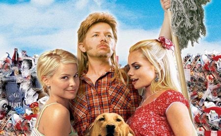 Fox Is Bringing Back Joe Dirt 25 Years Later With One Huge Change A man with a mullet stands between two blonde women, holding a mop, with a dog in front of him and a pile of trash in the background.