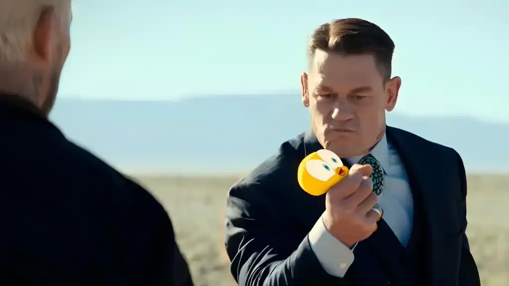 A man in a suit holds up a yellow smiley-face object with a serious expression while standing outdoors in a desert landscape.