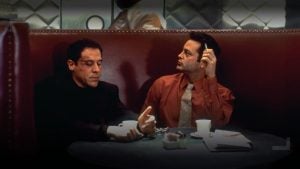 ‘Made’ 4K UHD Blu-Ray SteelBook Review – Favreau And Vaughn Reunite For Anxiety-Inducing Crime Comedy Two men sit in a red booth at a round table with coffee cups, sugar, and a newspaper. One man gestures with his hands while the other looks to the side, holding a cigarette.