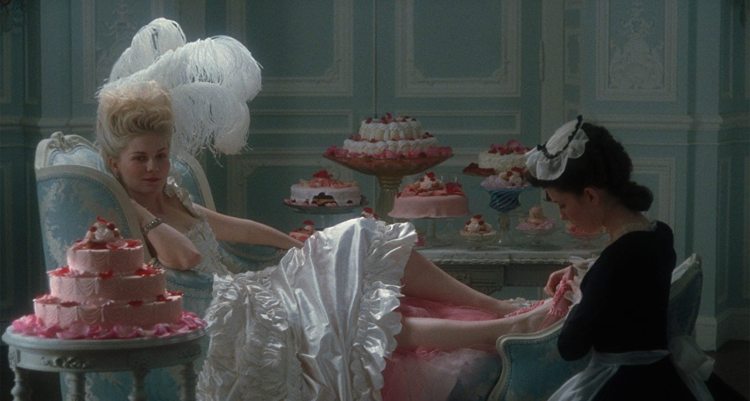 A woman in an elaborate white dress lounges on a blue chair, surrounded by cakes, while a maid tends to her feet in an ornate pastel room.