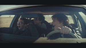 ‘Nimrods’ Review – A Charming if Somewhat Middling Coming-of-Age Comedy Three young men are in a moving car; one drives while the other two ride as passengers. They are smiling or laughing, and sunlight streams in through the windshield.