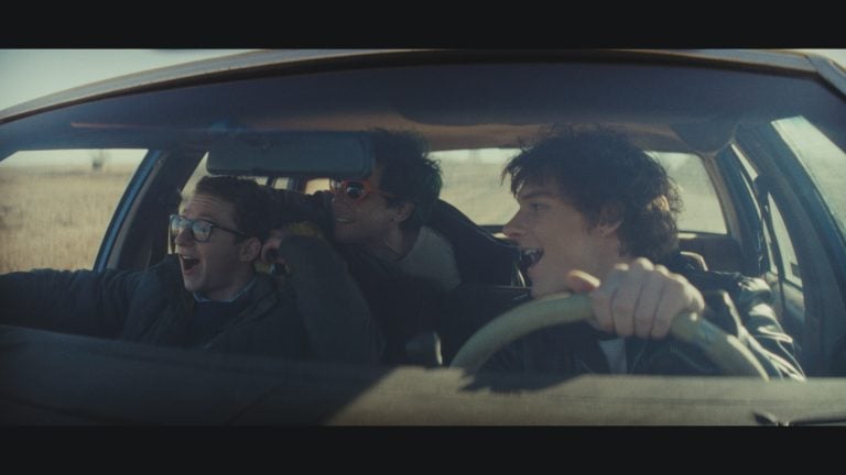 ‘Nimrods’ Review – A Charming if Somewhat Middling Coming-of-Age Comedy Three young men are in a moving car; one drives while the other two ride as passengers. They are smiling or laughing, and sunlight streams in through the windshield.