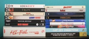 A stack of various DVD and Blu-ray movie cases, including titles like “Kill Bill,” “Identity,” and “Mars Attacks!” arranged in two columns against a turquoise background.