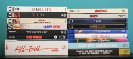 No Streaming Required: Physical Media Spotlight For The Week Of August 18th A stack of various DVD and Blu-ray movie cases, including titles like “Kill Bill,” “Identity,” and “Mars Attacks!” arranged in two columns against a turquoise background.
